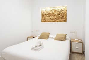 A neatly made bed with a white comforter and two pillows, a wall-mounted artwork, and bedside tables with lamps and a remote control. - Bajo Teatro Falla by Cadiz Time (Ciudad de Cádiz)