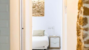 A bedroom with a bed, a nightstand, a lamp, and a textured wall art piece. - Bajo Teatro Falla by Cadiz Time (Ciudad de Cádiz)