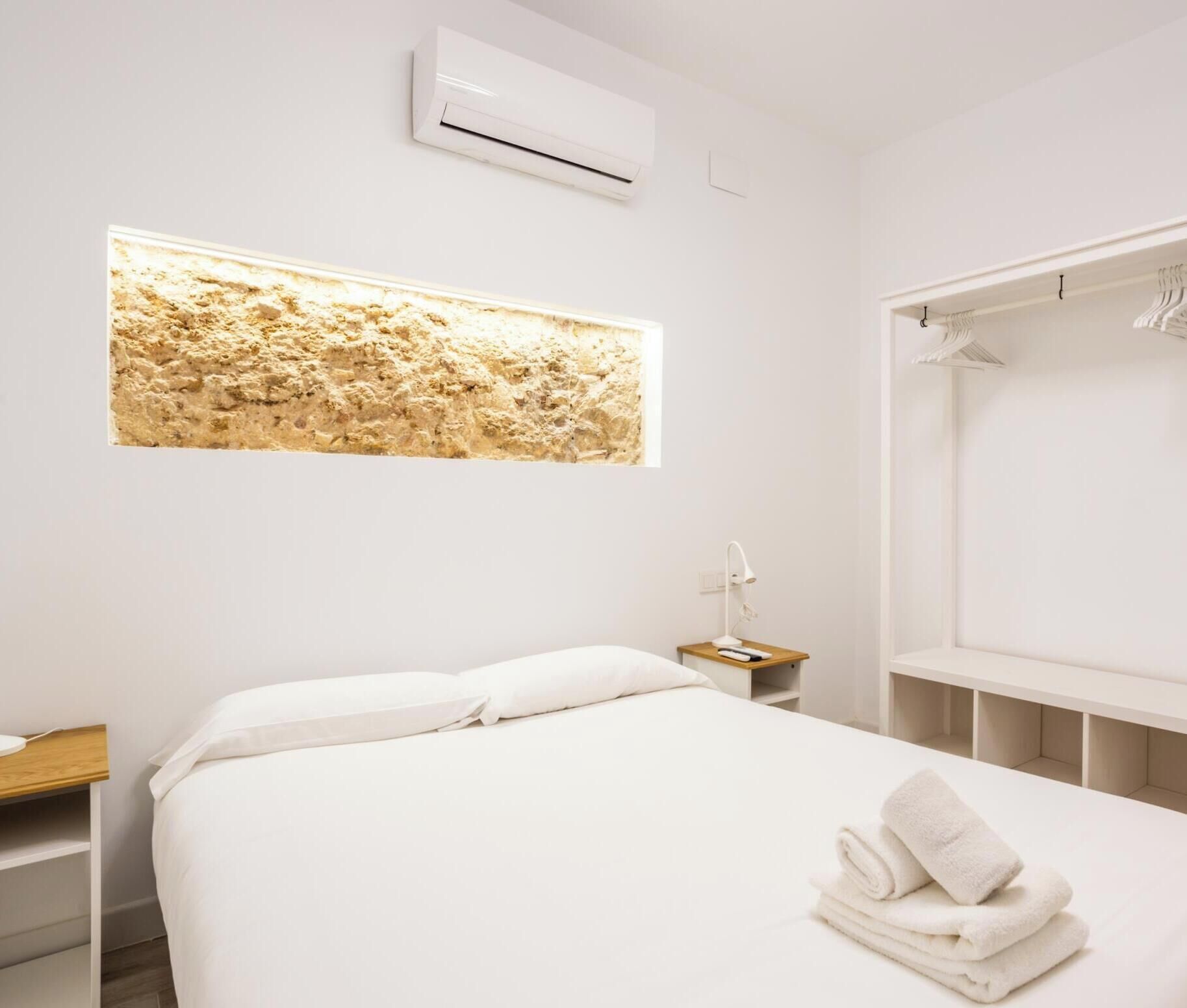 Une chambre d’hôtel moderne équipée d’un lit, d’une table de chevet, d’un climatiseur fixé au mur et d’une grande fenêtre offrant une vue intéressante.