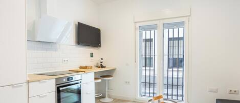 A compact kitchen with a built-in oven, a microwave, a small dining area with stools, and a large window with metal bars.