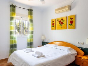 Ein Hotelzimmer mit einem Bett, einem Fenster mit Vorhängen, einer Klimaanlage und drei Bildern an der Wand.