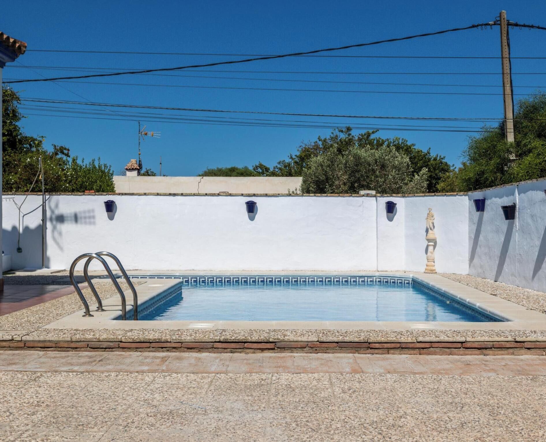 A rectangular swimming pool with a clear blue water surface, surrounded by a white wall with small windows and a decorative statue.