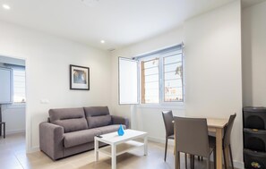 Ein modernes Wohnzimmer mit einem grauen Sofa, einem weißen Couchtisch und einem Essbereich mit einem Holztisch und Stühlen.