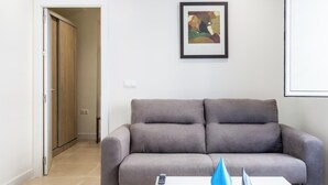 Una sala de estar con un sofá gris, una mesita de centro blanca, un jarrón azul y un cuadro en la pared.