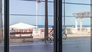 A coastal view through a window, including a beach, a white tent, a metal structure, and a tree. - Delfin Azul 2 FREE PARKING by Cadiz Time (Cádiz)