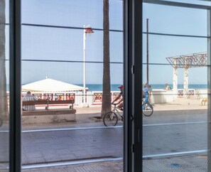 Blick auf die Küste durch ein Fenster, mit Strand, einem weißen Zelt, einer Metallkonstruktion und einem Baum.