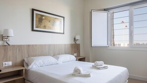 A hotel room with a bed, two bedside tables, a wall-mounted lamp, a framed picture, and a window with a view. - Delfin Azul 2 FREE PARKING by Cadiz Time (Cádiz)