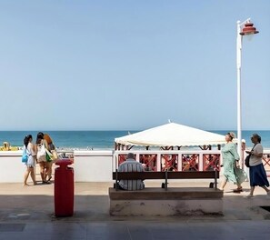 Ein Weg am Strand mit einer weißen Markise, einer Bank und einem Mülleimer.