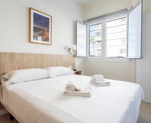 Ein Hotelzimmer mit Bett, Nachttisch, Fenster und einem gerahmten Bild an der Wand.
