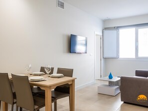 Ein modernes Wohnzimmer mit Essbereich, einem Flachbildfernseher, einer Couch und einem Fenster.