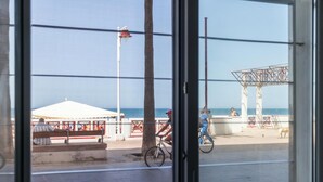 A coastal view through a window, including a beach, a white tent, a metal structure, and a tree. - Delfin Azul 3 by Cadiz Time (Cádiz)