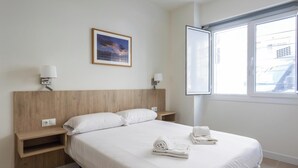 Habitación de hotel con una cama, dos mesitas de noche, una lámpara de noche, una ventana con persianas y un cuadro en la pared.