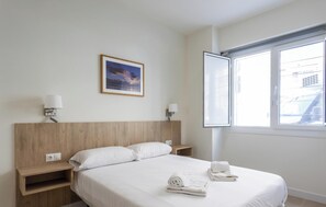 A hotel room with a bed, two bedside tables, a nightstand, a window with blinds, and a framed picture on the wall. - Delfin Azul 4 by Cadiz Time (Cádiz)