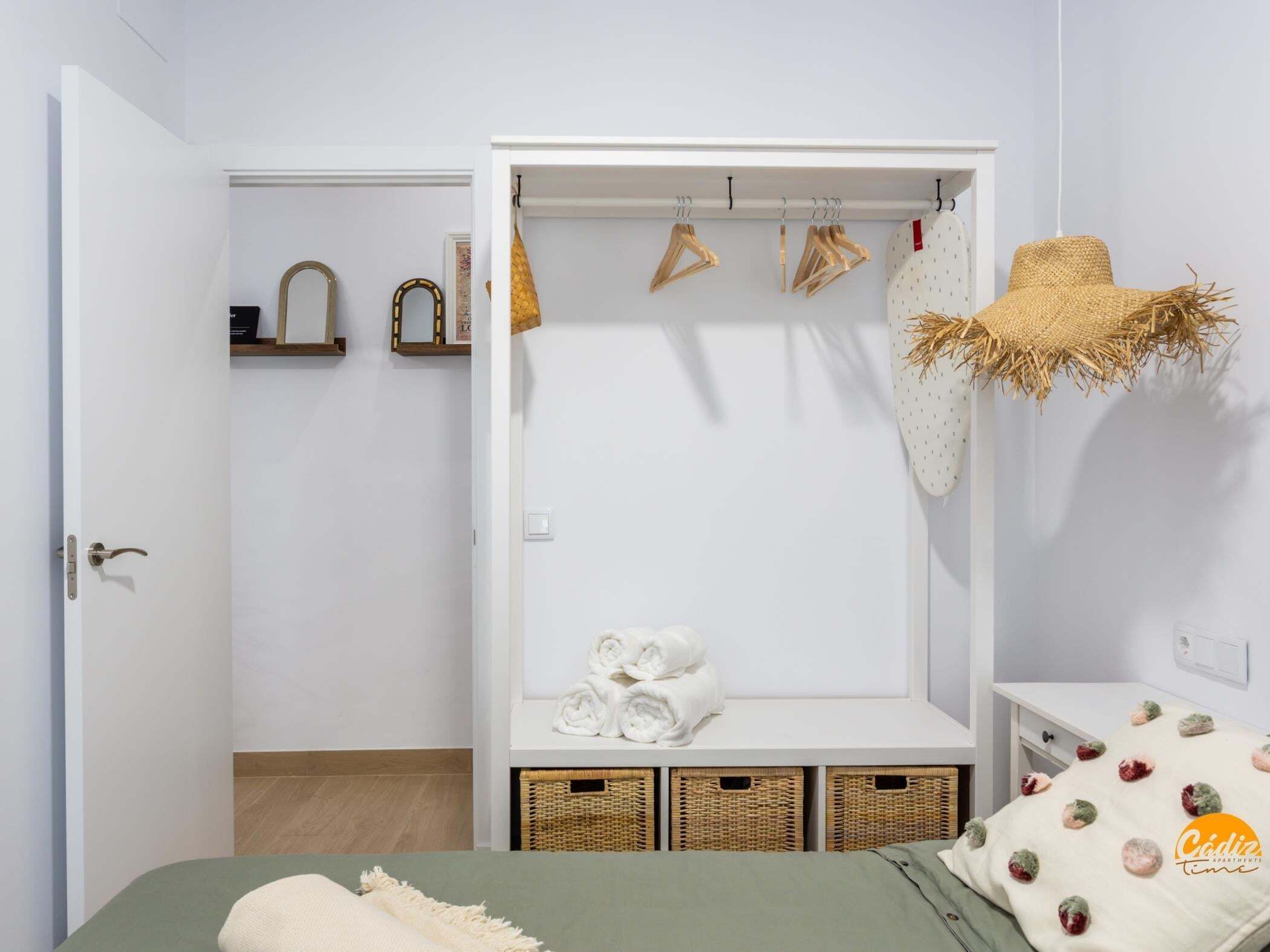 Een slaapkamer met een bed, een kledingkast, een ophangrek met kleding en een mand.