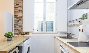 Eine moderne Küche mit Steinrückwand, integriertem Waschmaschine, Kaffeemaschine und einem Fenster mit Jalousien.