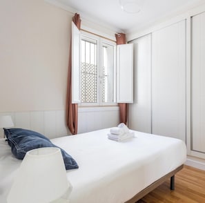 Ein Schlafzimmer mit Bett, Lampe, einem Fenster mit Vorhängen und einem Kleiderschrank.