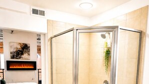 Un bagno moderno con cabina doccia in vetro, un camino a muro e un letto nella stanza adiacente.