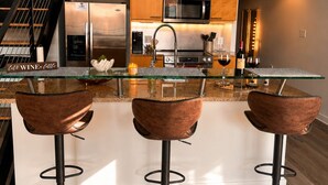 Una cucina moderna con un'isola in vetro, elettrodomestici in acciaio inossidabile e tre sgabelli da bar.