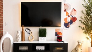 Un soggiorno moderno con una TV a schermo piatto montata a parete, un mobile TV nero con spazio contenitore, una pianta in vaso e una statuetta decorativa di un ghepardo.