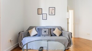 En stue med en grå sofa, et glasbord og tre billeder i rammer på væggen.