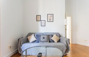 Ein Wohnzimmer mit grauem Sofa, einem Glastisch und drei gerahmten Kunstwerken an der Wand.