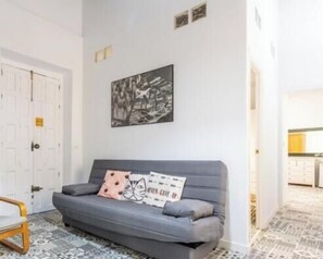 Ein Zimmer mit einer grauen Couch, einem Schwarz-Weiß-Kunstwerk an der Wand und einem gemusterten Boden.