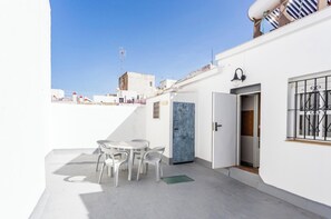 Eine Dachterrasse mit Tisch, Stühlen, einer Tür und einem Fenster mit Gitterstäben.