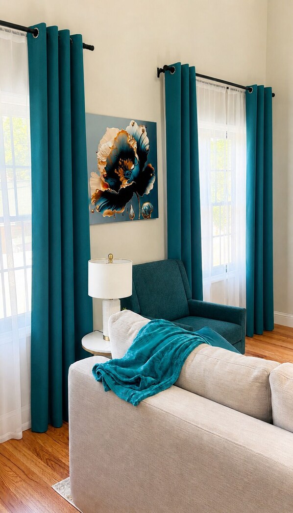 A living room with teal curtains, a teal armchair, a white sofa, a lamp, and a wall painting. - 2 Apts, 2bd 2ba, Sleeps 10, Clean & Reliable, Near NYC (Scotch Plains)