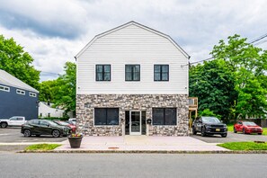A two-story building with a stone facade, a front entrance, and a visible garage door. - 2 Apts, 2bd 2ba, Sleeps 10, Clean & Reliable, Near NYC (Scotch Plains)