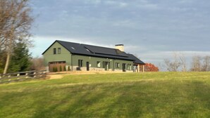 Un edificio verde con techo inclinado y chimenea, rodeado de un campo cubierto de hierba y árboles.