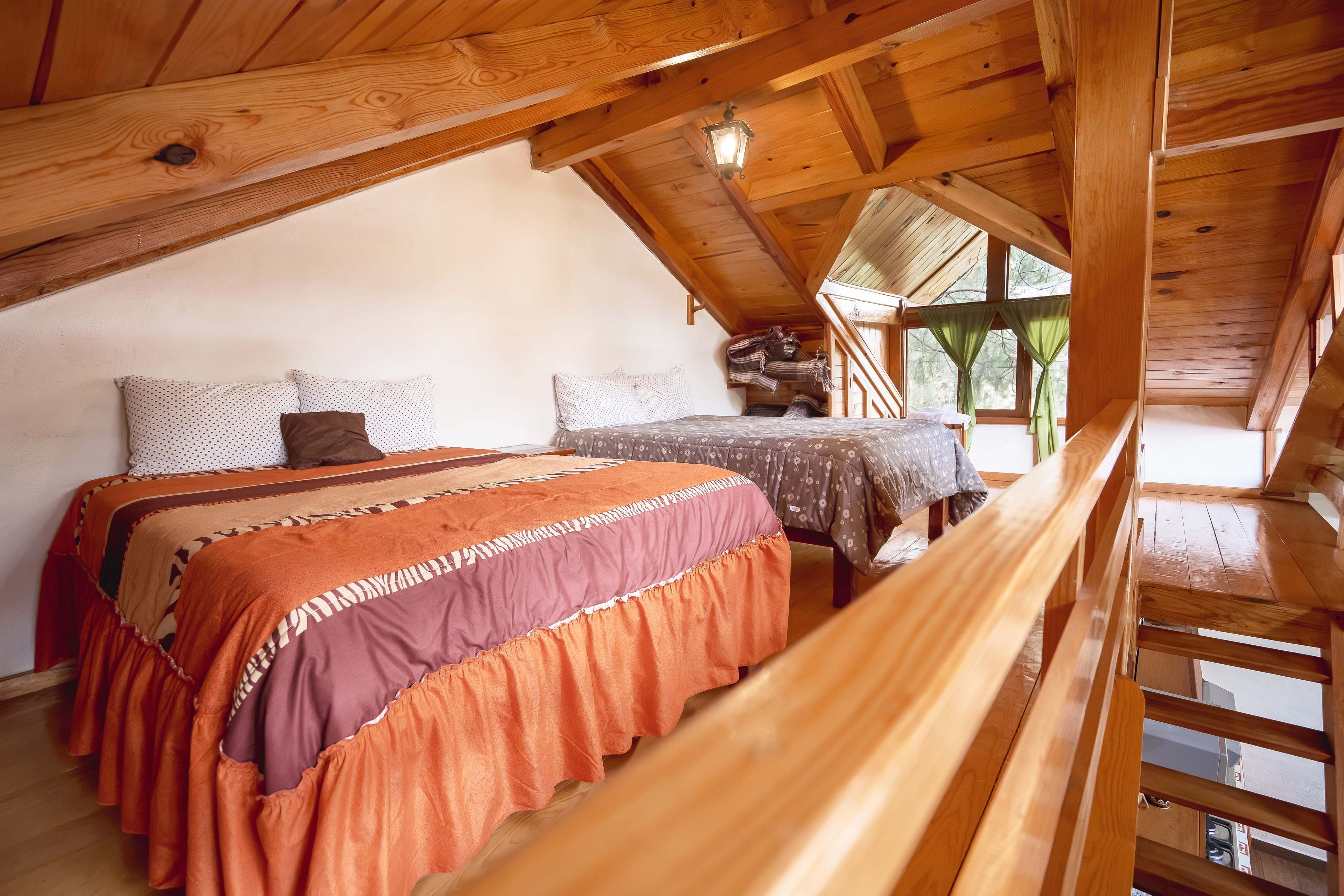 Un dormitorio acogedor en el ático con techo de madera, una cama con ropa de cama estampada y vistas al exterior a través de una ventana.