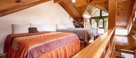 Un dormitorio acogedor en el ático con techo de madera, una cama con ropa de cama estampada y vistas al exterior a través de una ventana.