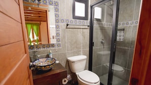 A bathroom with a toilet, a sink with a decorative bowl, a shower area, and a window with curtains. - Paseo del Llano Cabañas & Suites (Mazamitla)