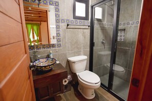 A bathroom with a toilet, a sink with a decorative bowl, a shower area, and a window with curtains. - Paseo del Llano Cabañas & Suites (Mazamitla)