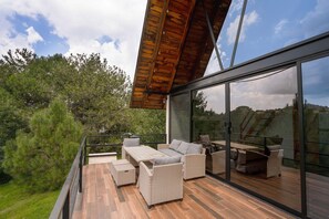 A modern outdoor deck with wicker furniture and a glass enclosure. - Paseo del Llano Cabañas & Suites (Mazamitla)