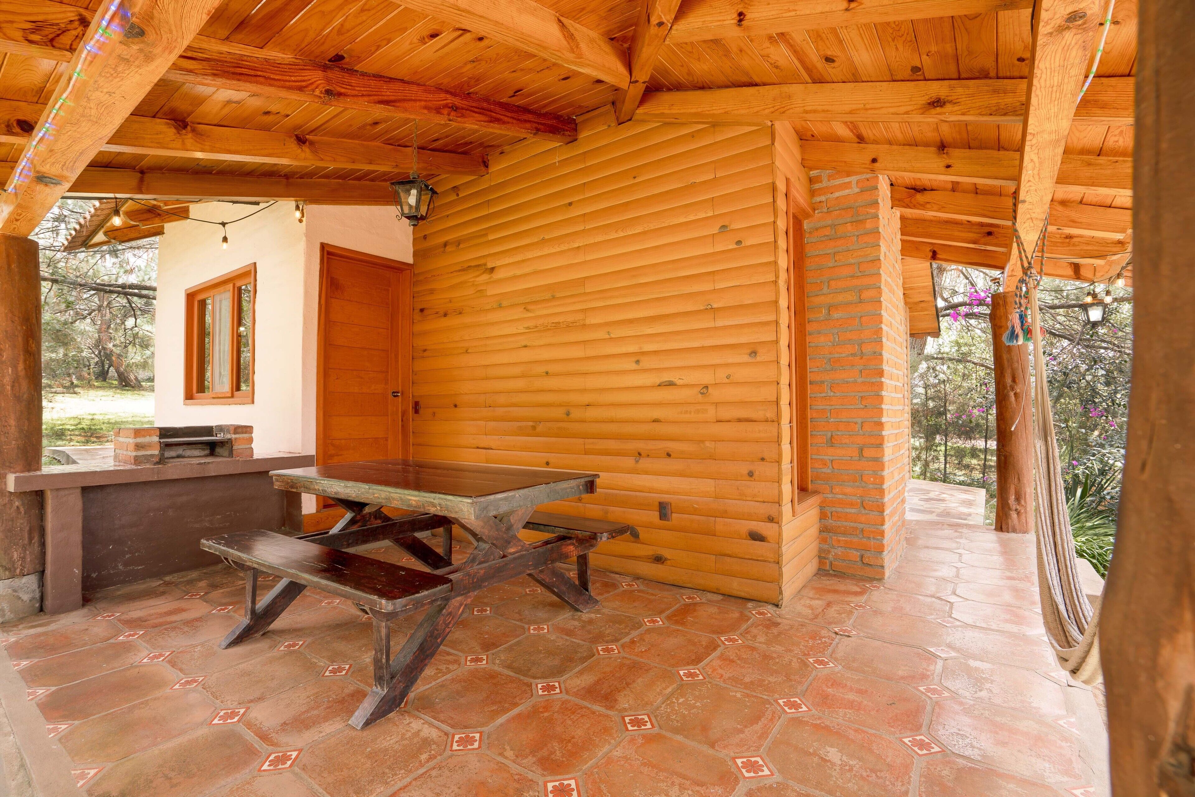 A wooden cabin with a stone-tiled patio, a wooden table, and a brick fireplace.
