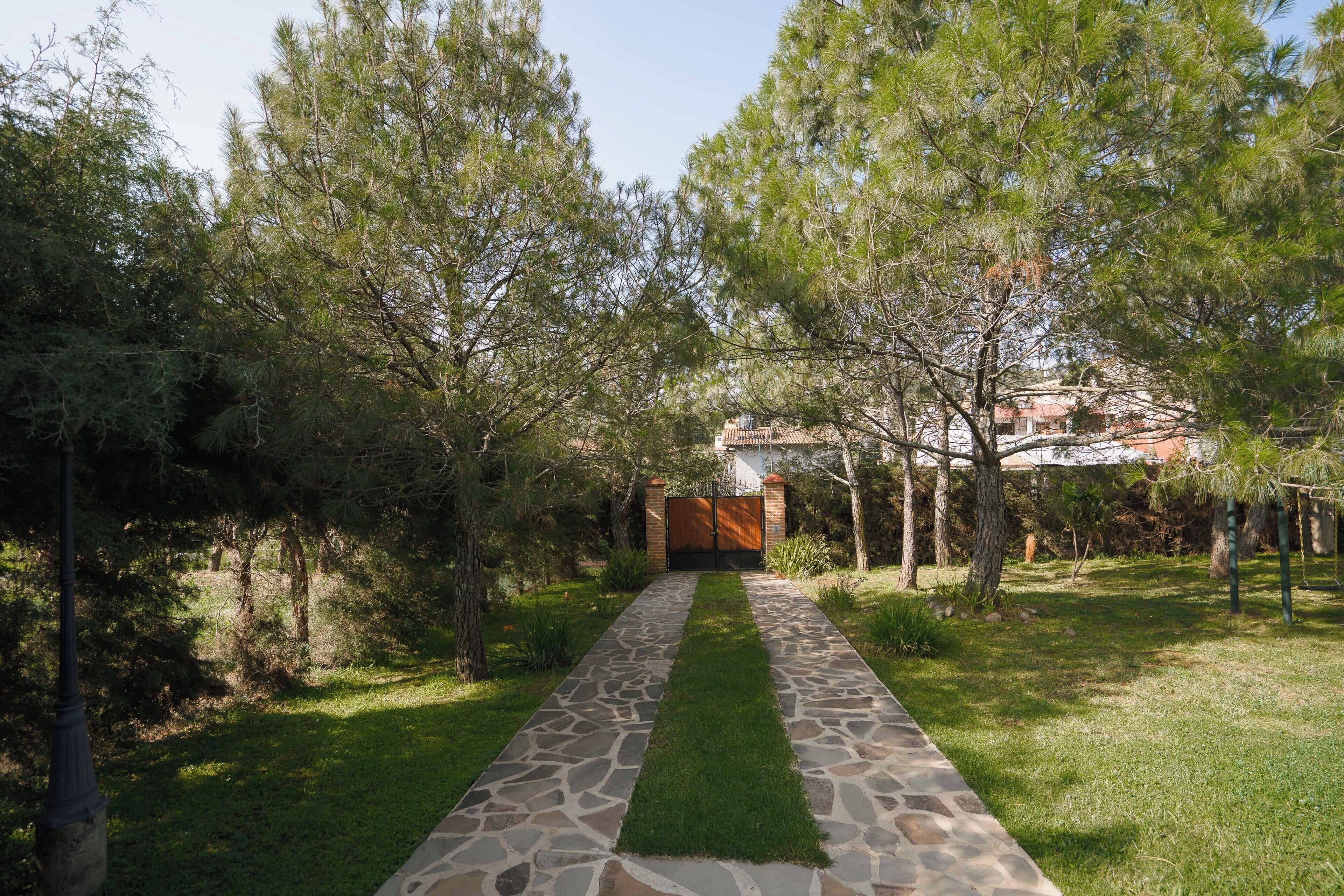 Un sendero de piedra que conduce a una entrada con puerta de hierro, rodeada de árboles.