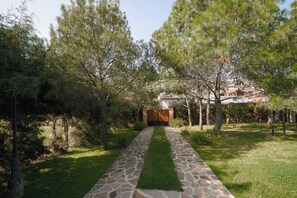 Un sendero de piedra que conduce a una entrada con puerta de hierro, rodeada de árboles.
