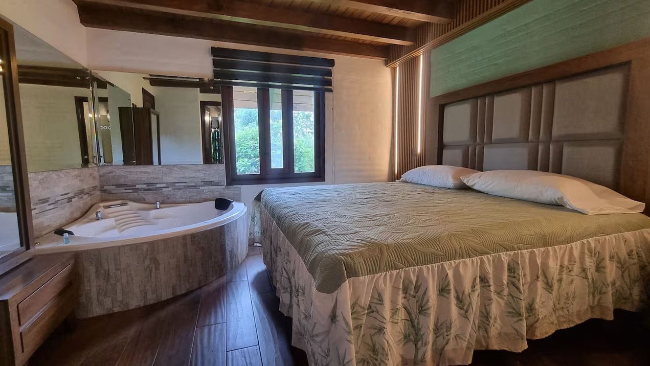 A bedroom with a large bed, a bathtub, and a window with a view of greenery.