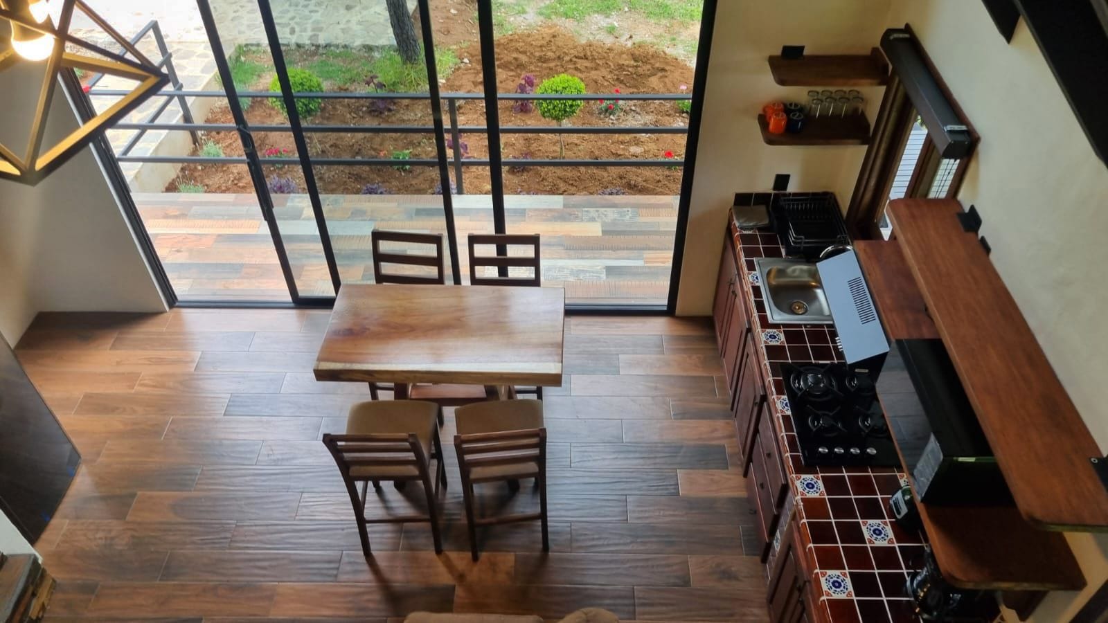 A kitchen with a wooden table and chairs, a stove, and a view of a garden through a glass door.