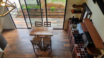 A kitchen with a wooden table and chairs, a stove, and a view of a garden through a glass door.