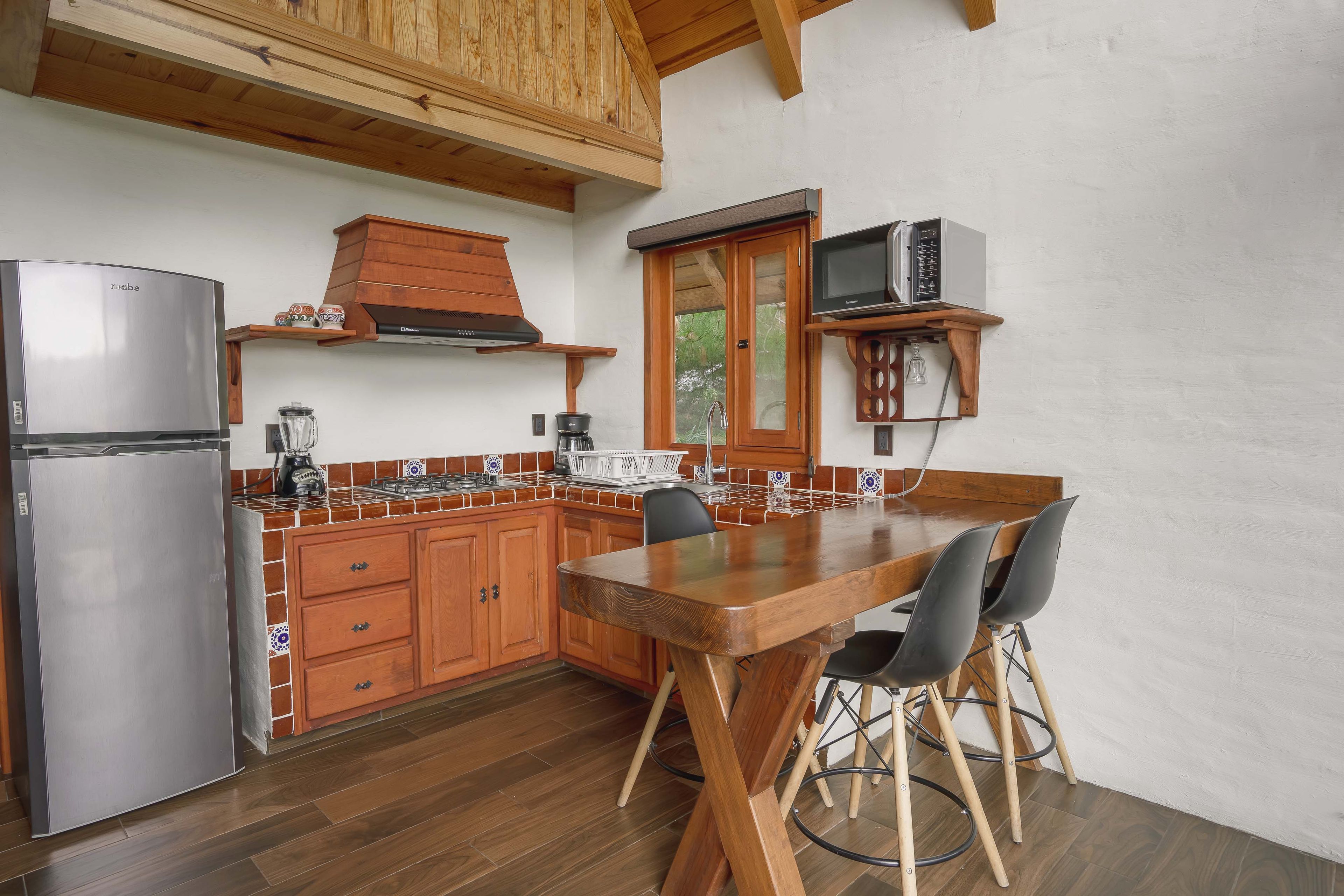 Una cocina con gabinetes de madera, un refrigerador de acero inoxidable, una cafetera y una mesa de comedor con sillas.