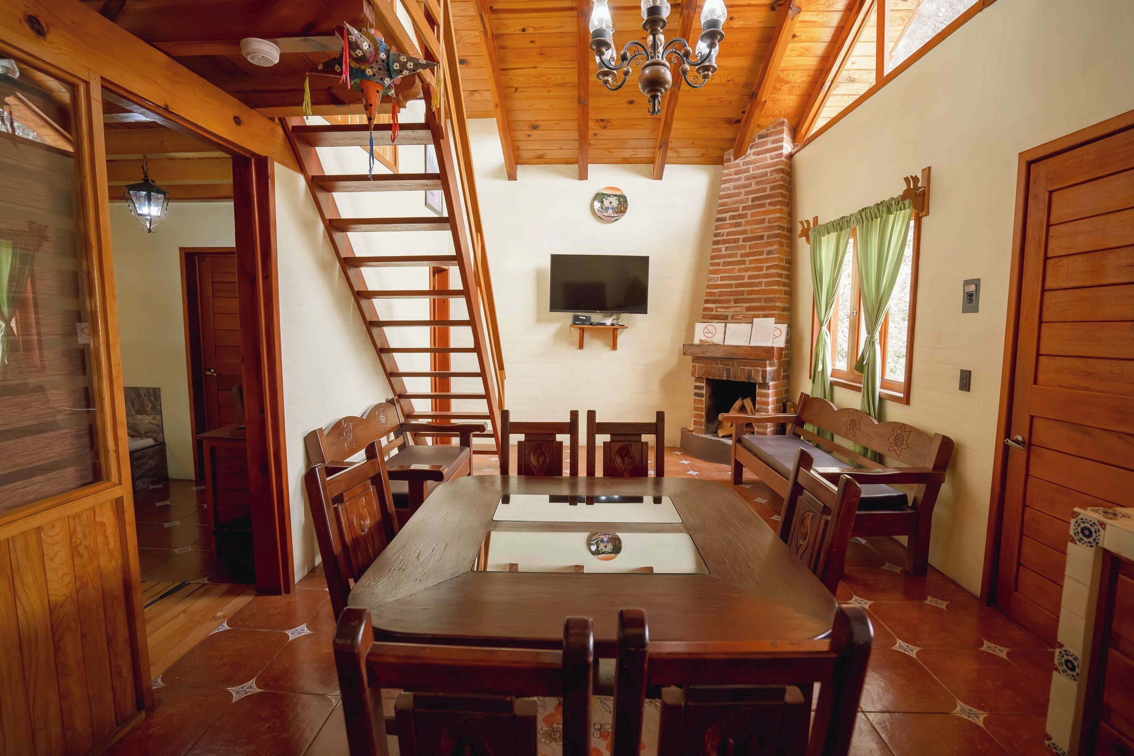 A wooden interior with a dining table, chairs, a TV, and a fireplace.
