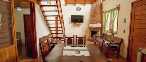 A wooden interior with a dining table, chairs, a TV, and a fireplace.