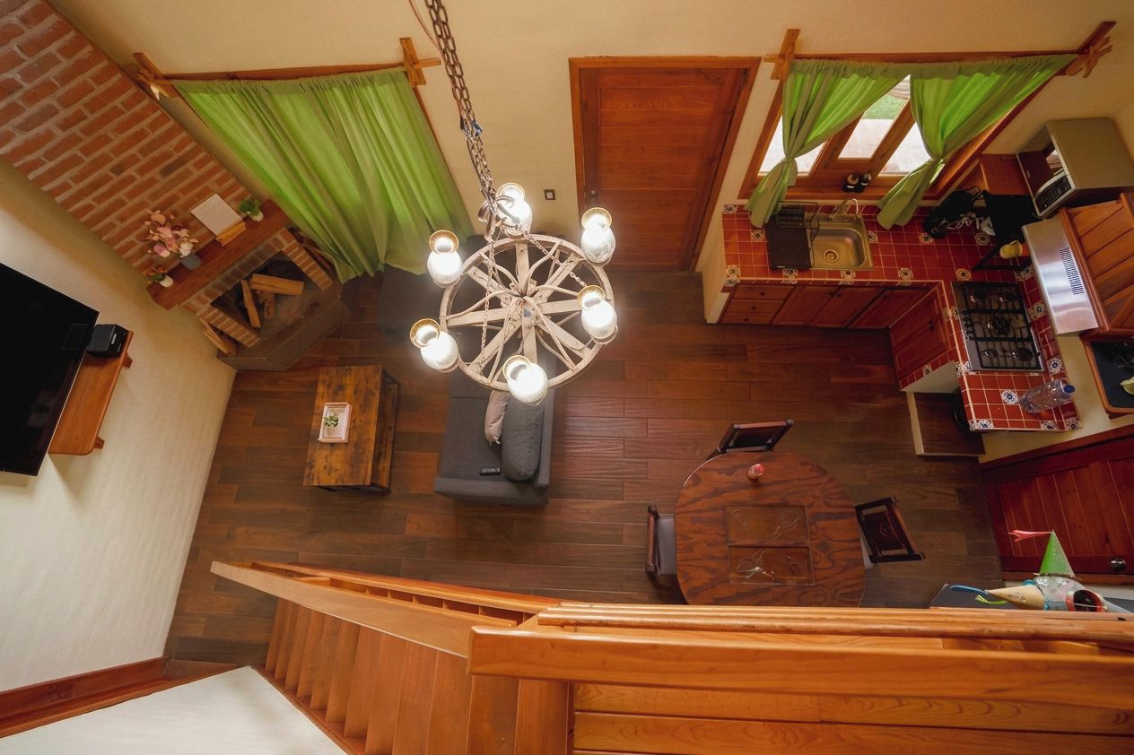 Un interior acogedor con una escalera de madera, chimenea, zona de comedor y cocina con lámpara colgante.