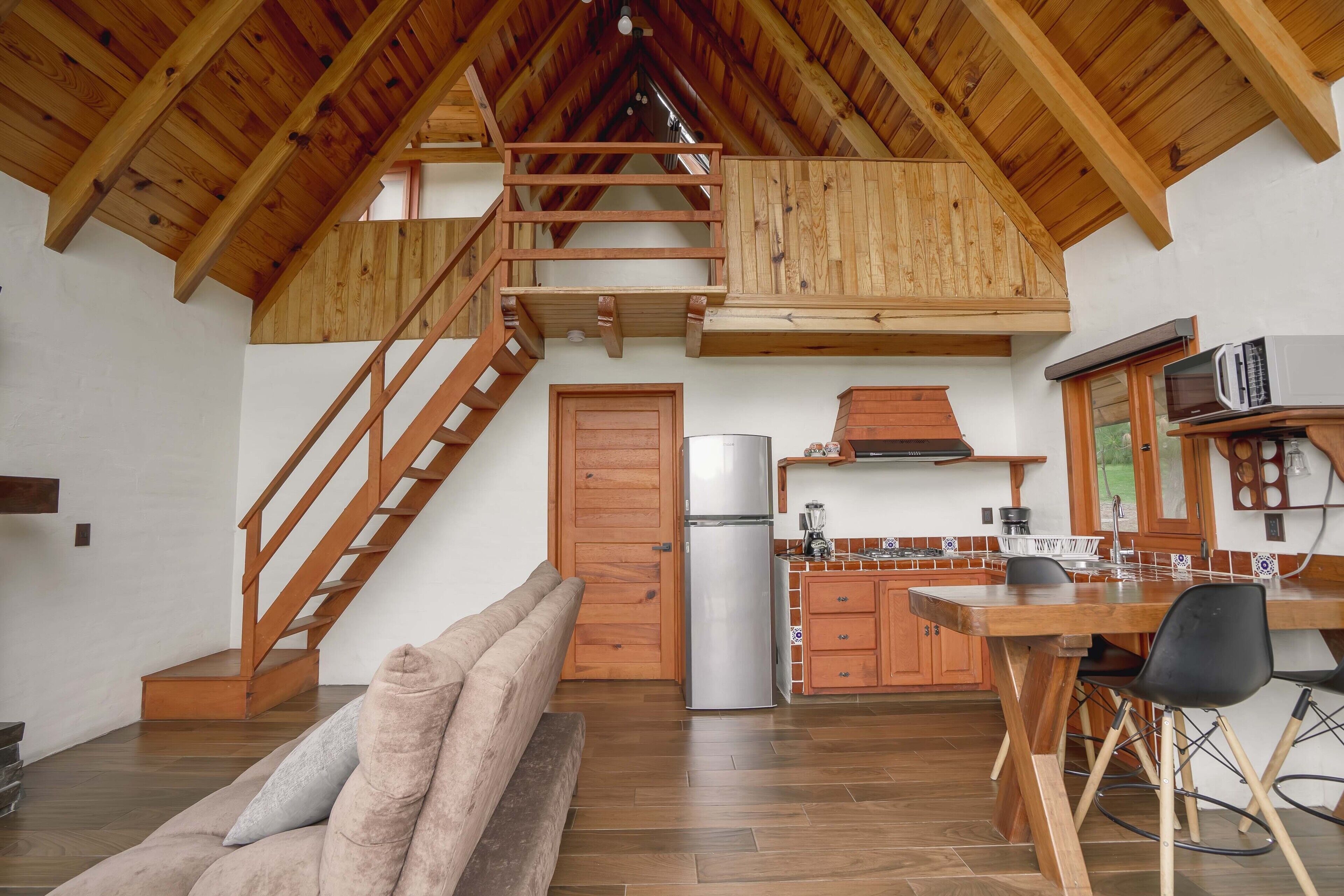 A modern kitchen with a wooden staircase, a dining area with a table and chairs, and a cozy seating area with cushions.
