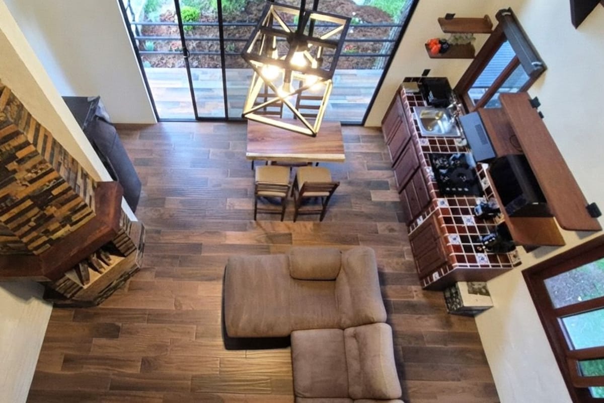 Amplia sala de estar con piso de madera, un sofá, una mesa de comedor y una cocina con horno empotrado.