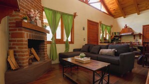 A cozy living room with a brick fireplace, green curtains, a sofa, and a wooden coffee table. - Paseo del Llano Cabañas & Suites (Mazamitla)