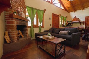 A cozy living room with a brick fireplace, green curtains, a sofa, and a wooden coffee table. - Paseo del Llano Cabañas & Suites (Mazamitla)