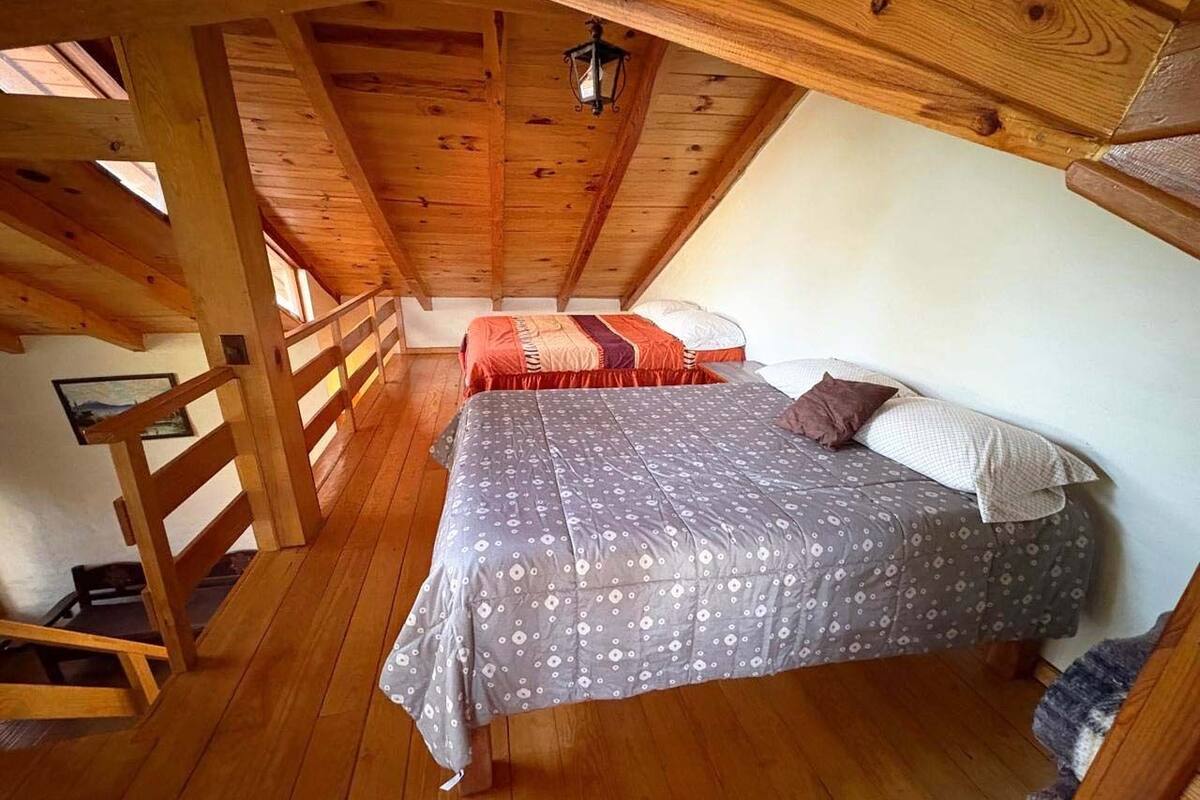 Ett sovrum på ett öppet loftplan, inrett med en säng, en extra säng och en trappa i trä.